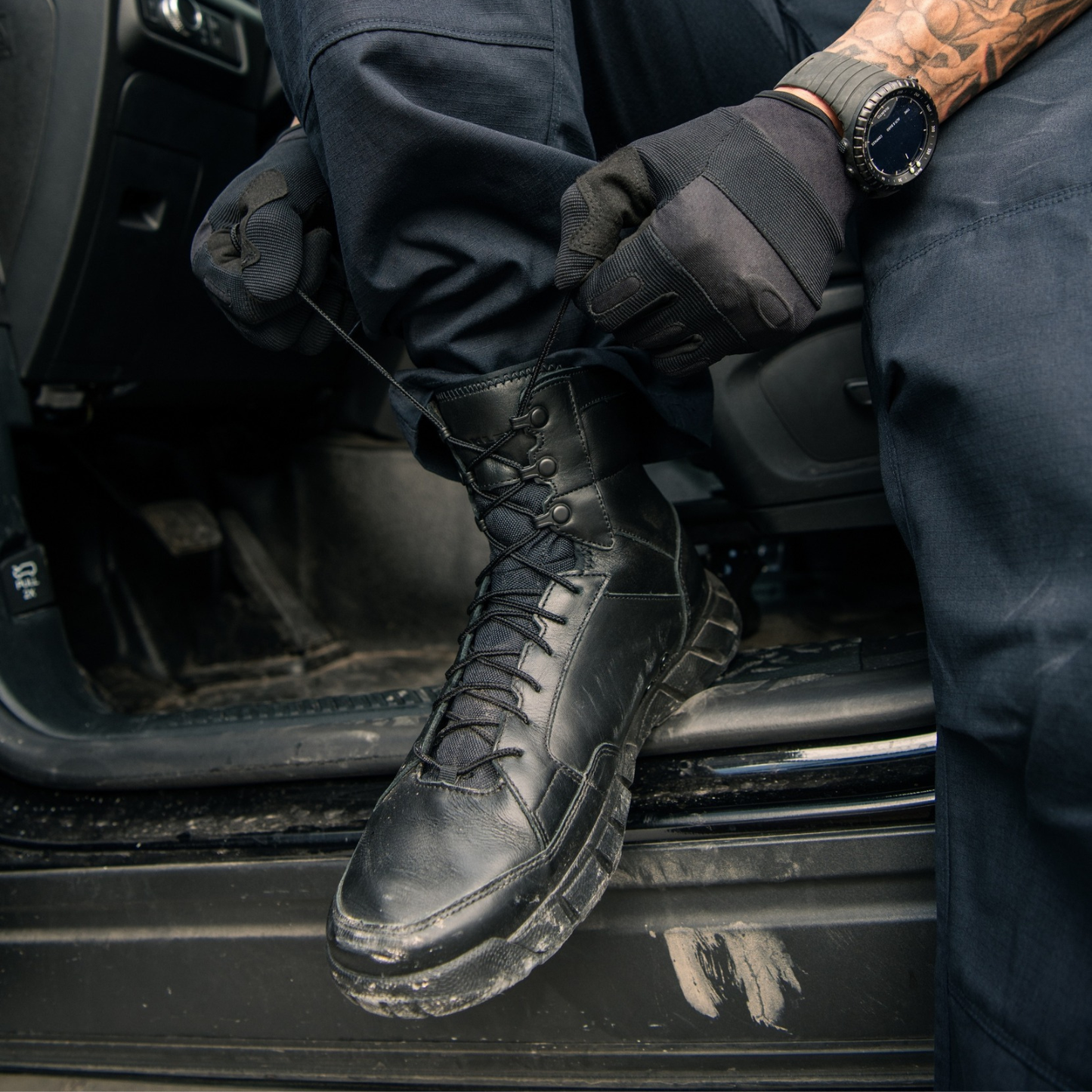 Officer in tactical gear and Oakley boots in a police patrol vehicle