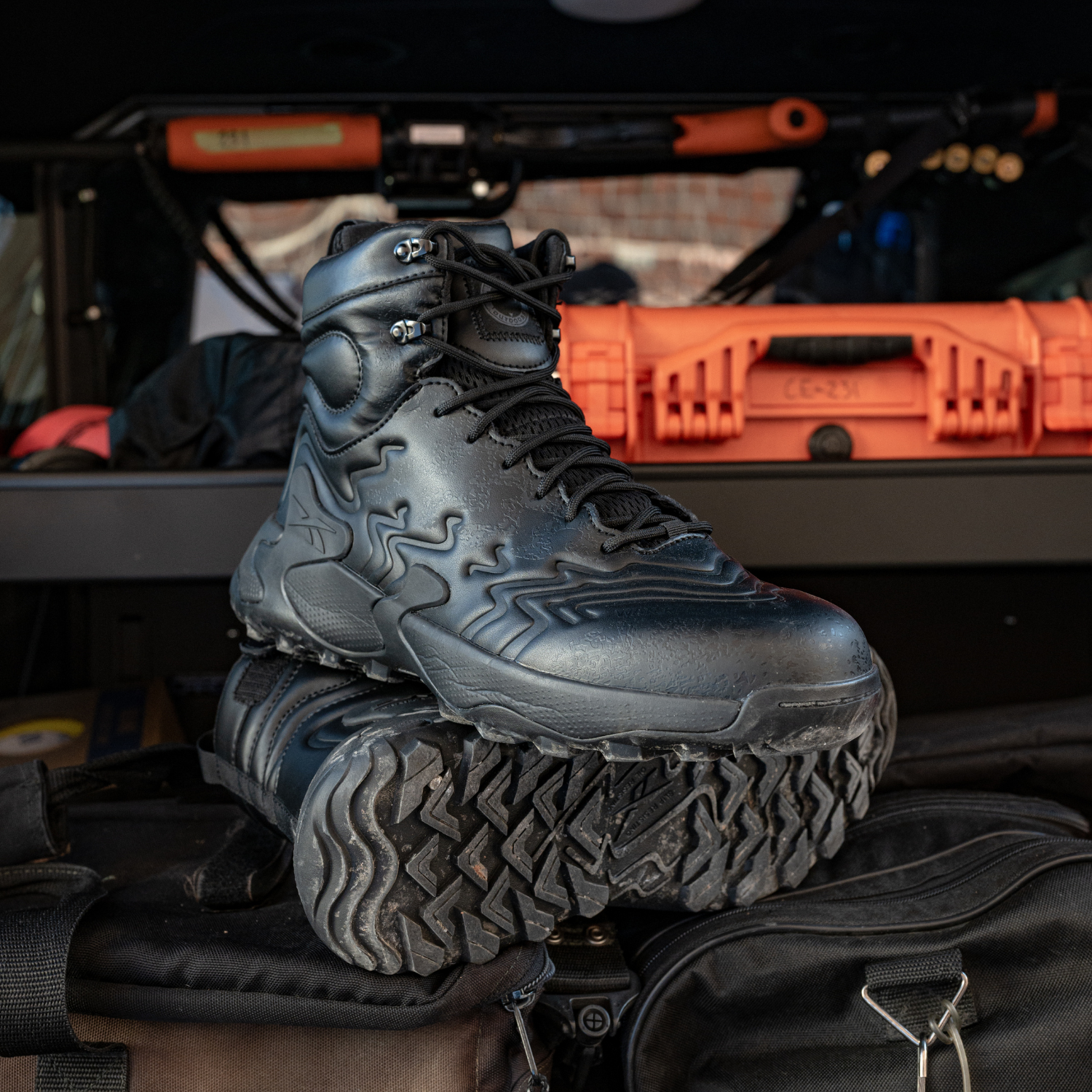 Black tactical boot with orange toolbox and vehicle in the background
